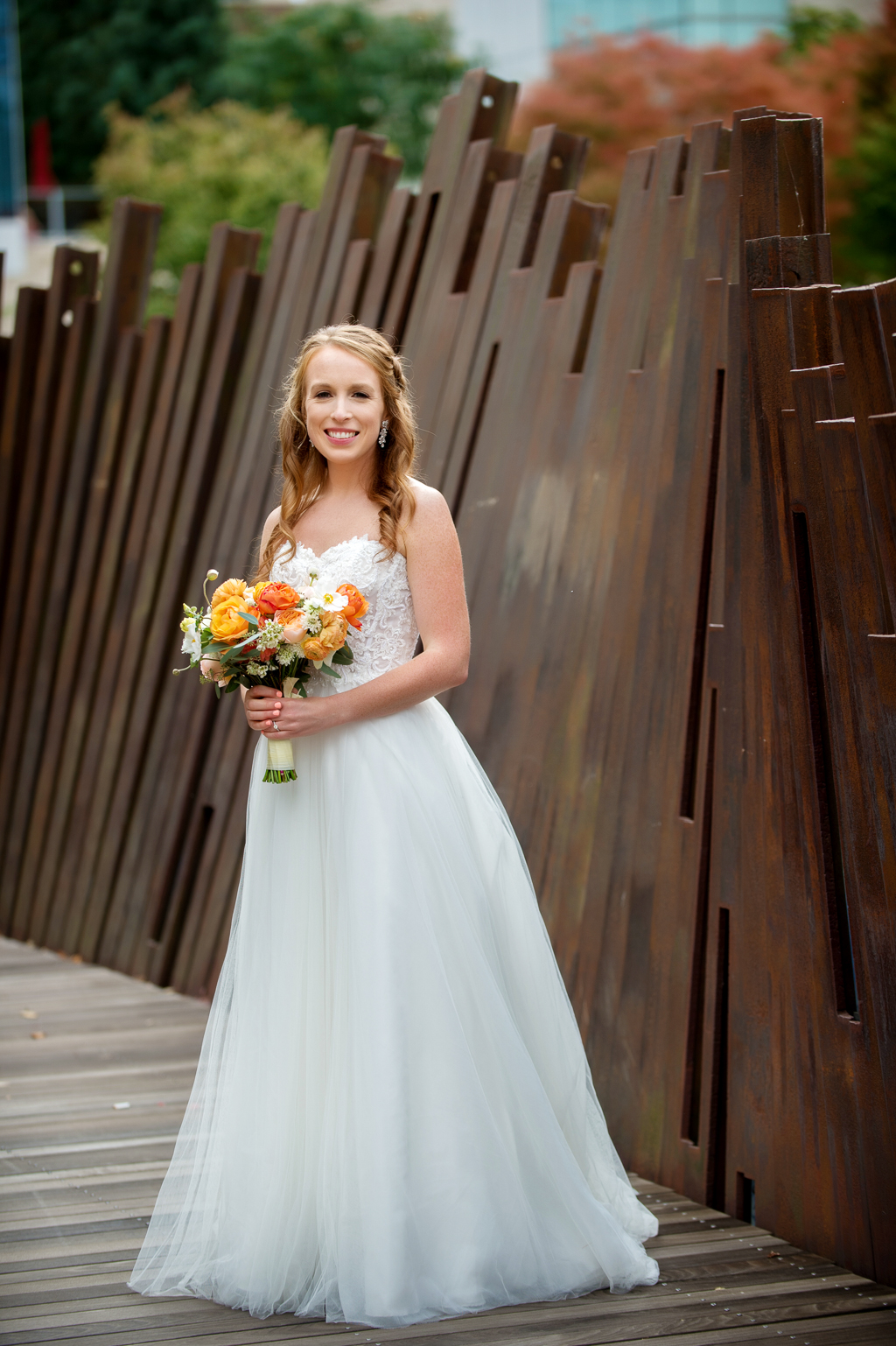 bride stands along boardwalk in front of rusty fence sculpture wall at tanner springs park