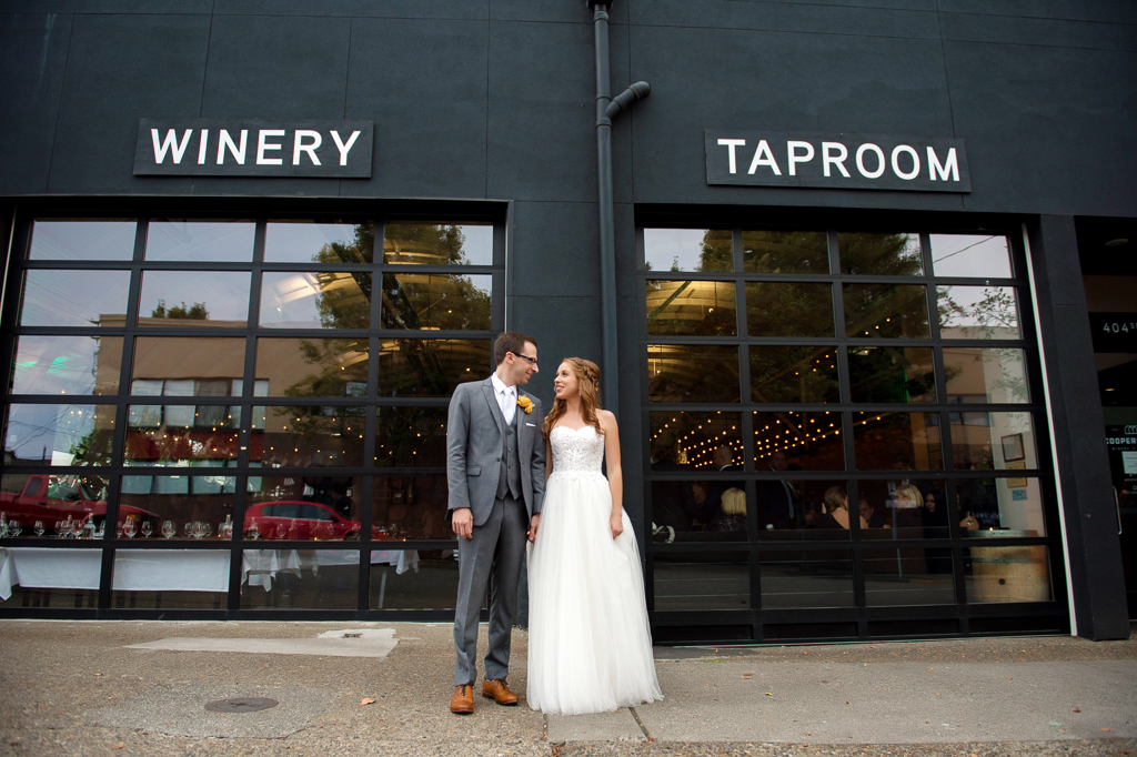 a bride and groom stand outside of coopers hall winery taproom looking at each other