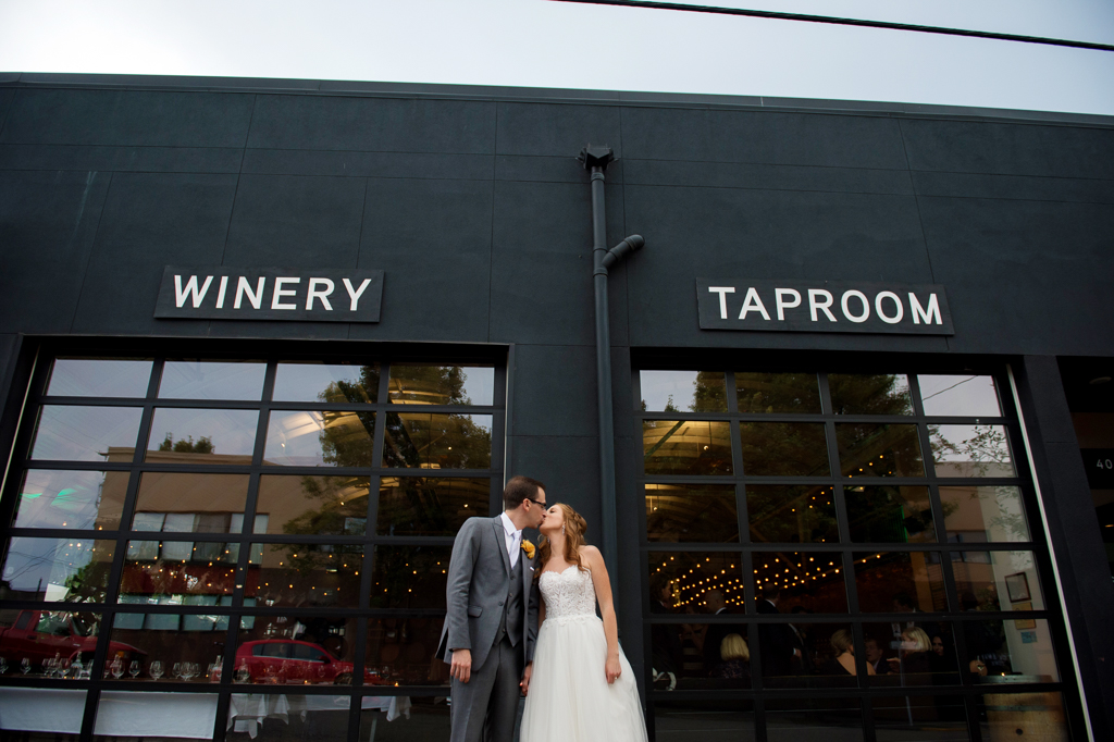 a bride and groom kiss in front of coopers hall winery taproom wall