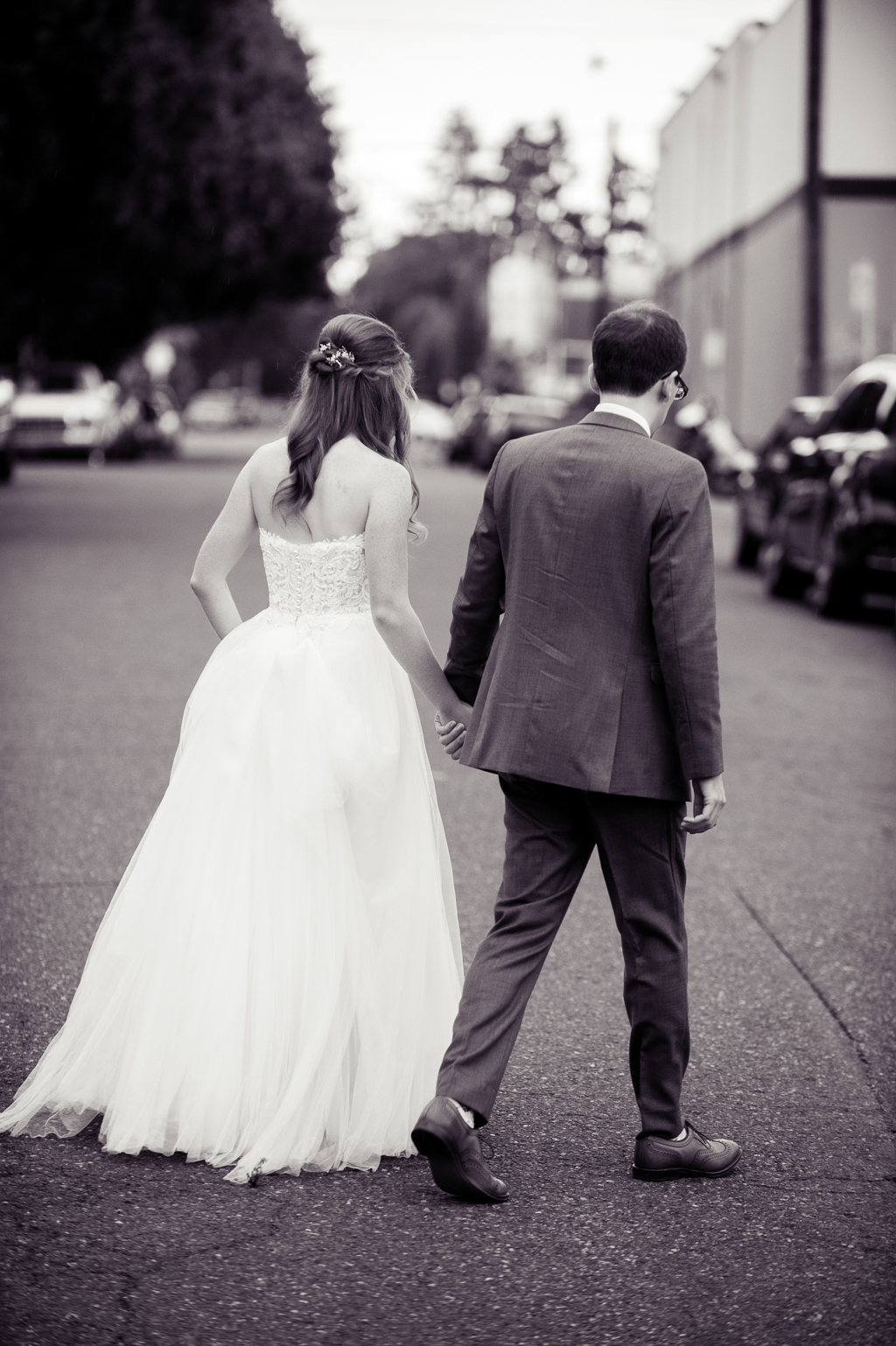 a bride and groom walk hand in hand down the middle of a street in portland