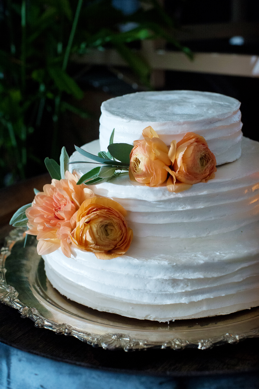 a 3 tier wedding cake adorned with orange peach ranunculus