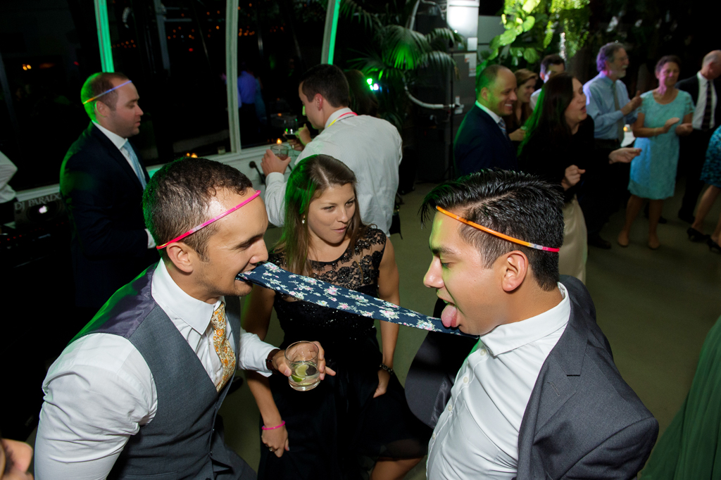 a man dances with another man's tie in his mouth at a wedding reception