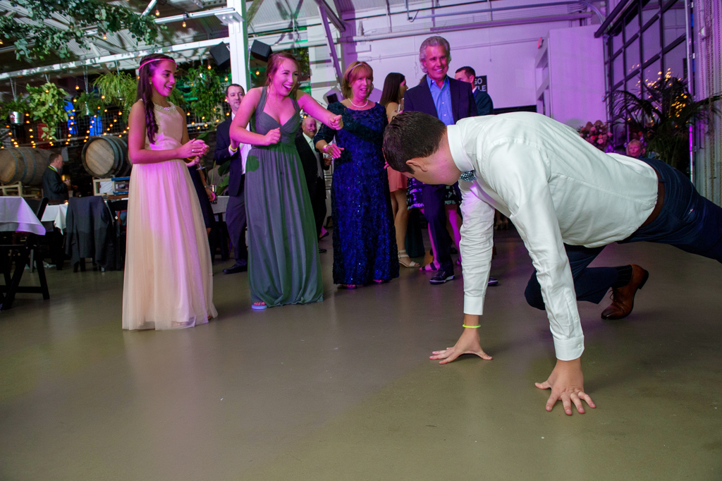 a bridesmaid points in shock at her boyfriend who is dancing on all fours at a wedding reception