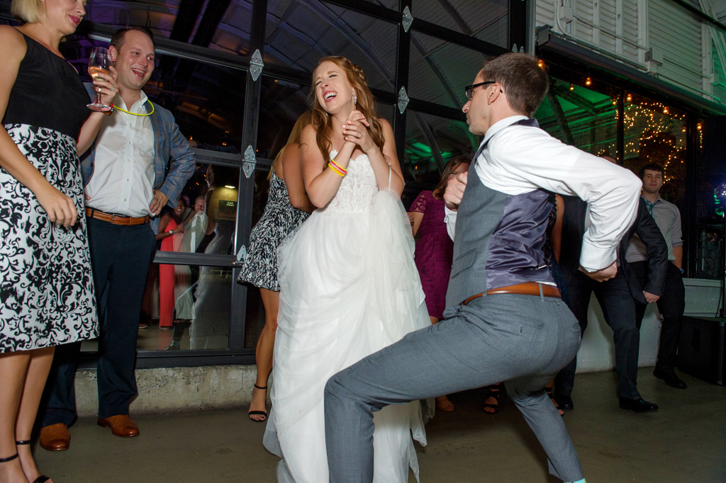 a bride laughs at her groom who is dancing silly at the wedding reception