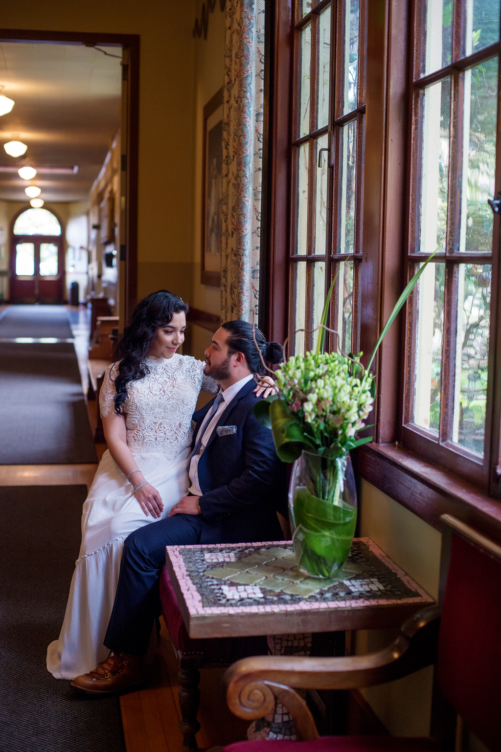a bride sits on a grooms lap in the hallway at kennedy school