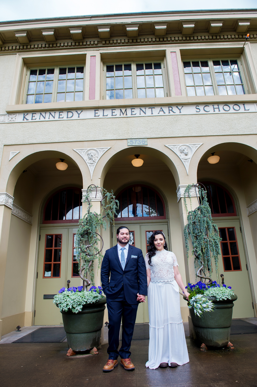 bride and groom stand side by side outside the front entrance of kennedy school