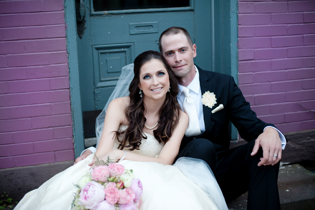 a bride and groom sit on a stoop in front of a purple wall and teal door