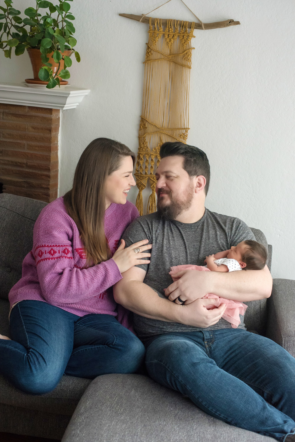 a mom and dad sit on their couch in their home holding their newborn baby girl