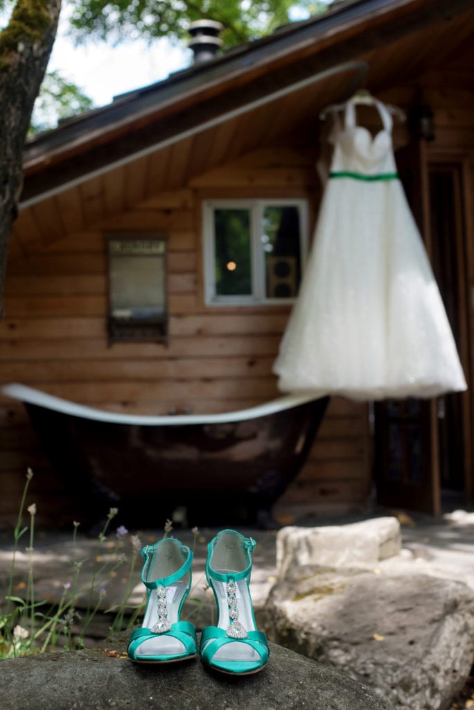 emerald green wedding shoes sit on a rock in the foreground and a wedding dress hangs in the background
