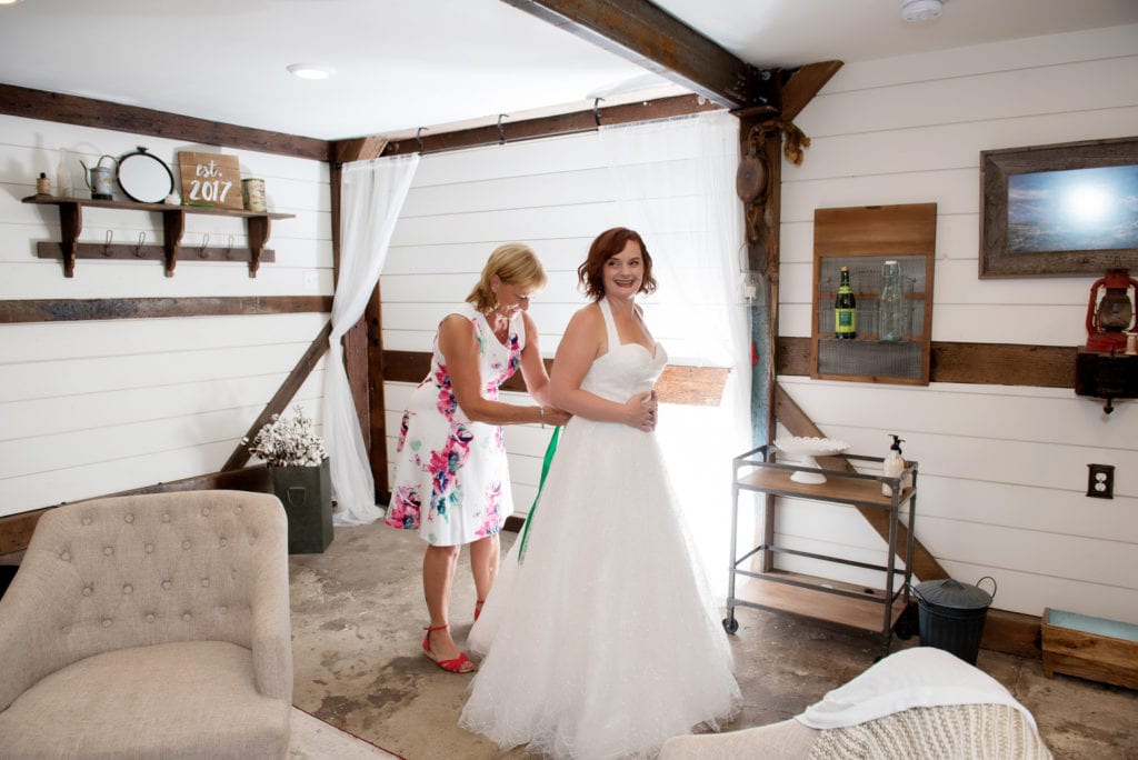 a mom helps the bride into her wedding dress 
