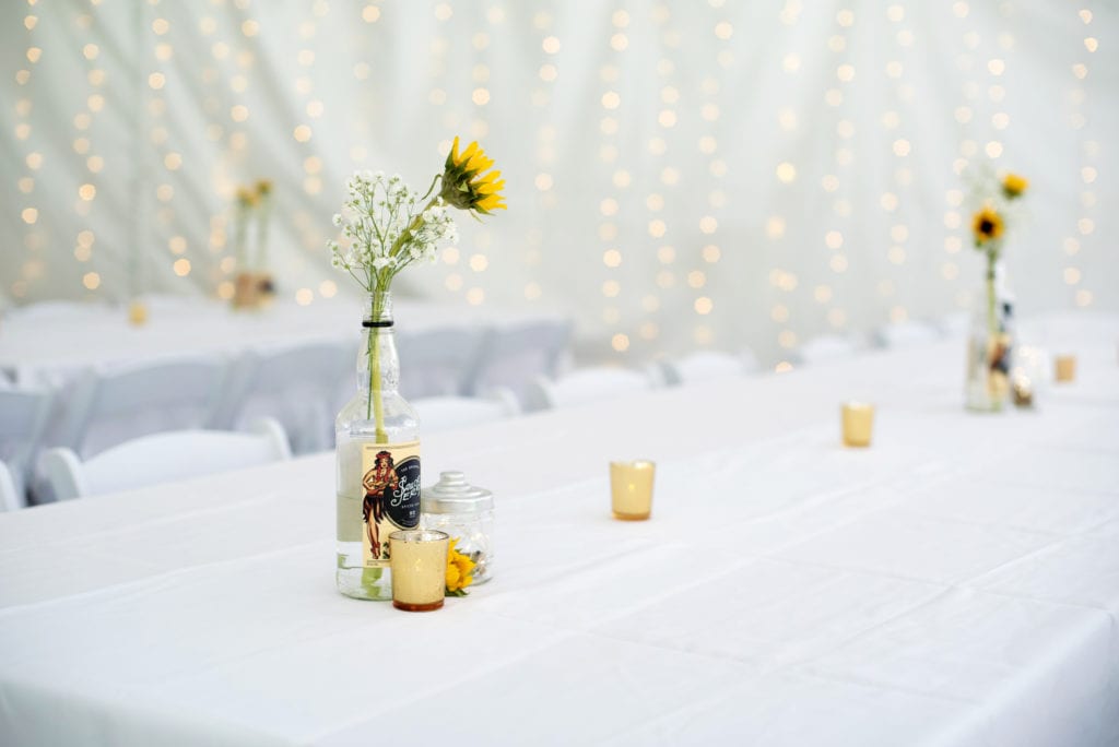 sunflowers and babys breath in rum bottles, line the tables at a reception
