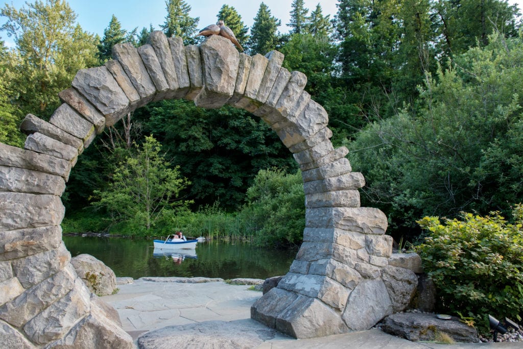 a bride and groom in a rowboat can be seen through the stone arch 
