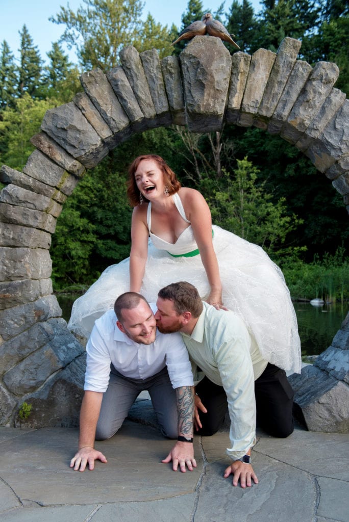 a bride and two men create a human pyramid under the stone arch 