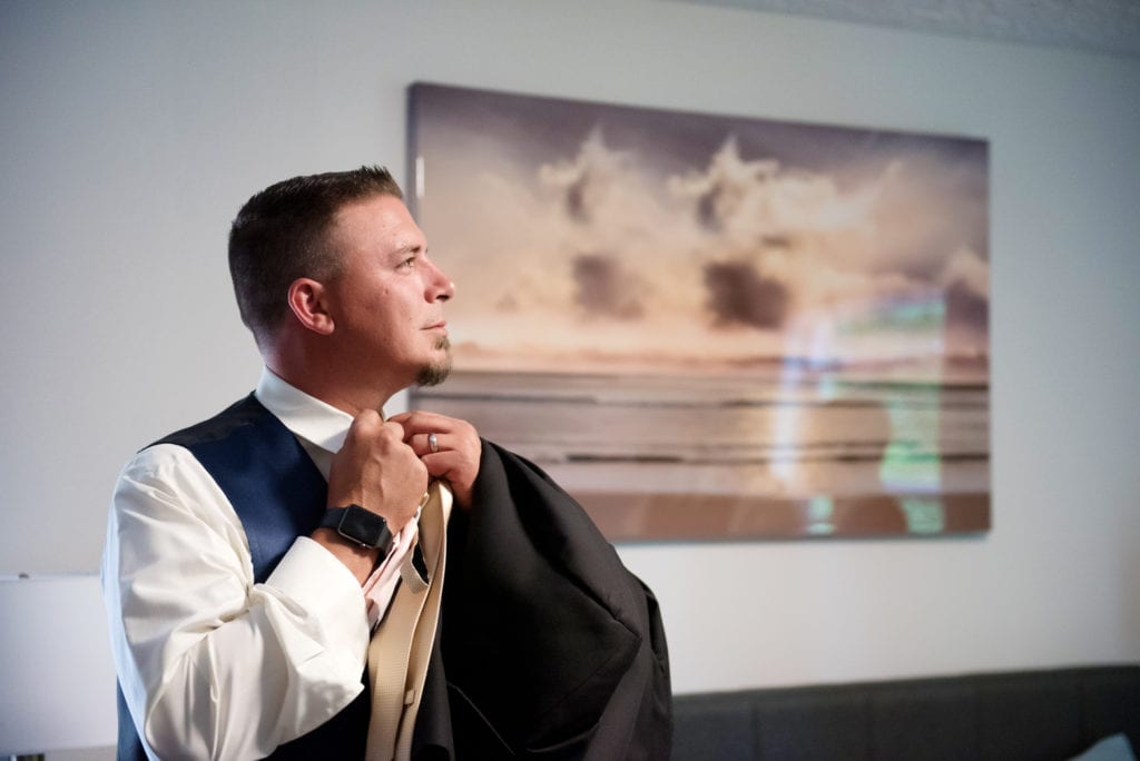 groom gets ready in front of an ocean portrait hanging on the wall
