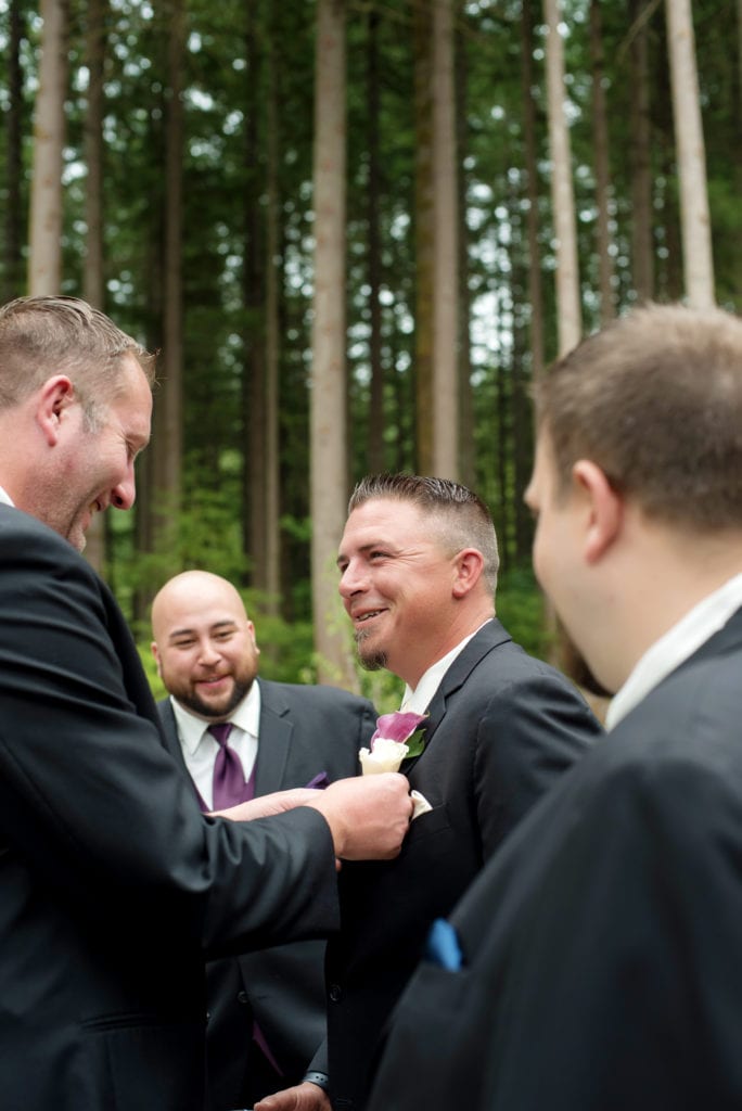 groomsmen laugh as they help groom with boutonniere 