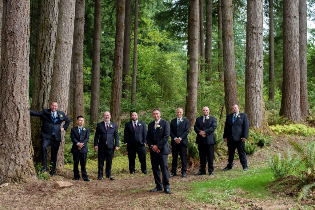 groomsmen in navy and purple stand underneath large trees
