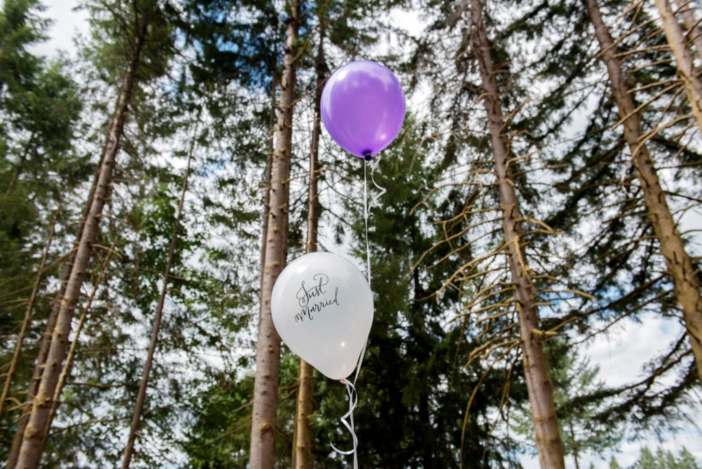 purple balloon and a white balloon that says just married float against very tall trees
