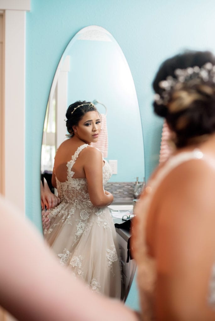 bride looks over her shoulder into a mirror at her wedding dress