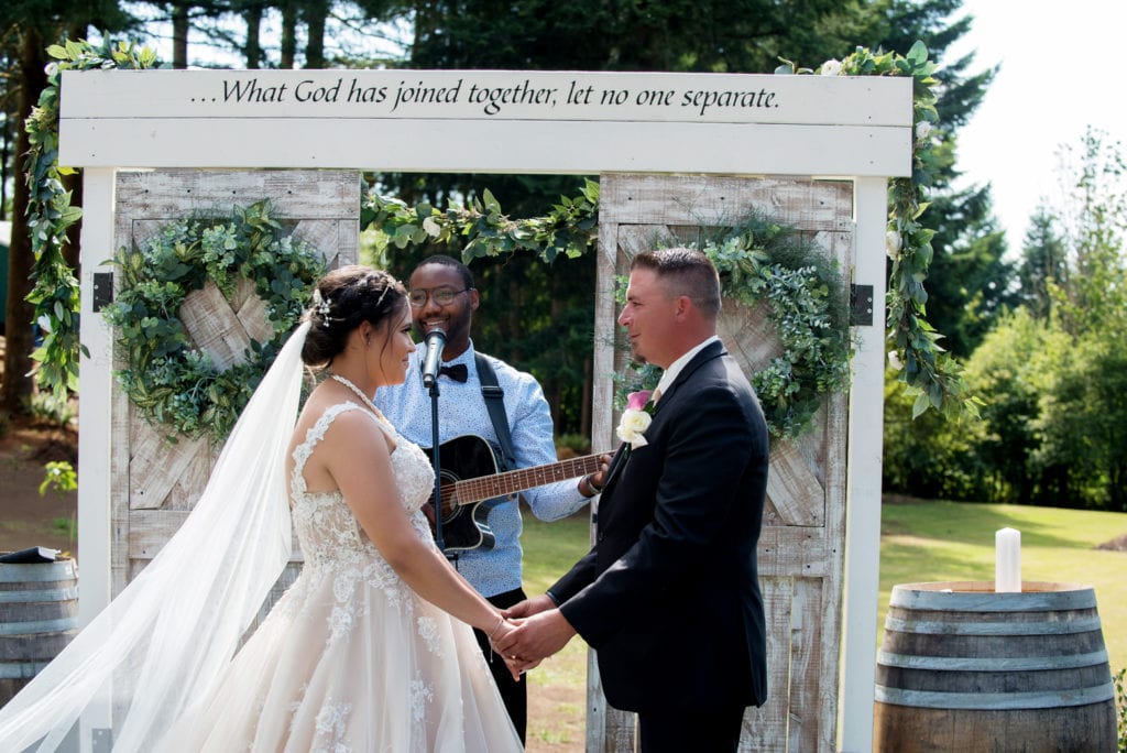 a bride and groom stand in front of a cute arbor make out of wooden doors with "what god has joined together, let no one separate" written above
