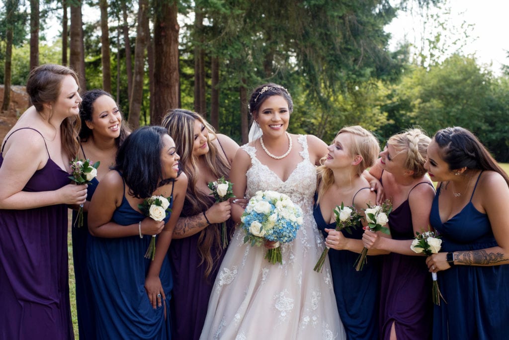bridesmaids in purple and navy dresses hug around the bride