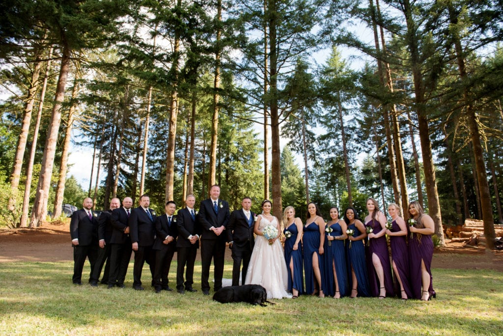 bridesmaids and groomsmen in purple and navy dresses and vests stand around the bride