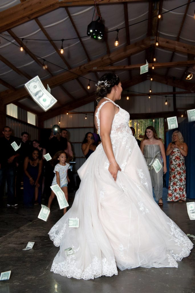 a bride in a large white wedding dress spins around as lots of dollar bills rain down around her