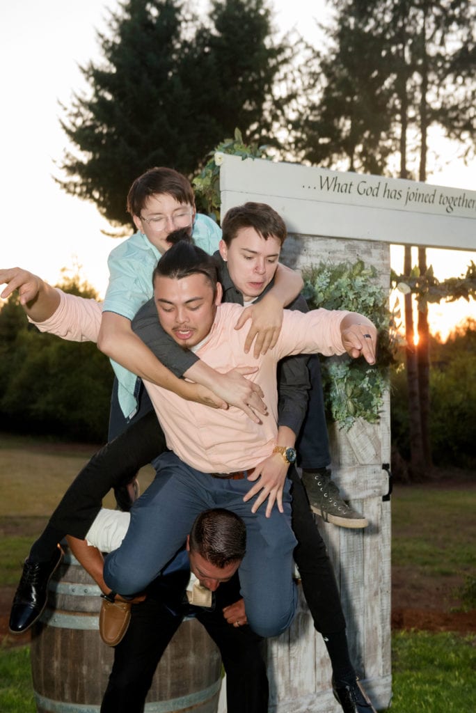 a groom's 3 adult sons climb onto his shoulders and then they all start to fall over