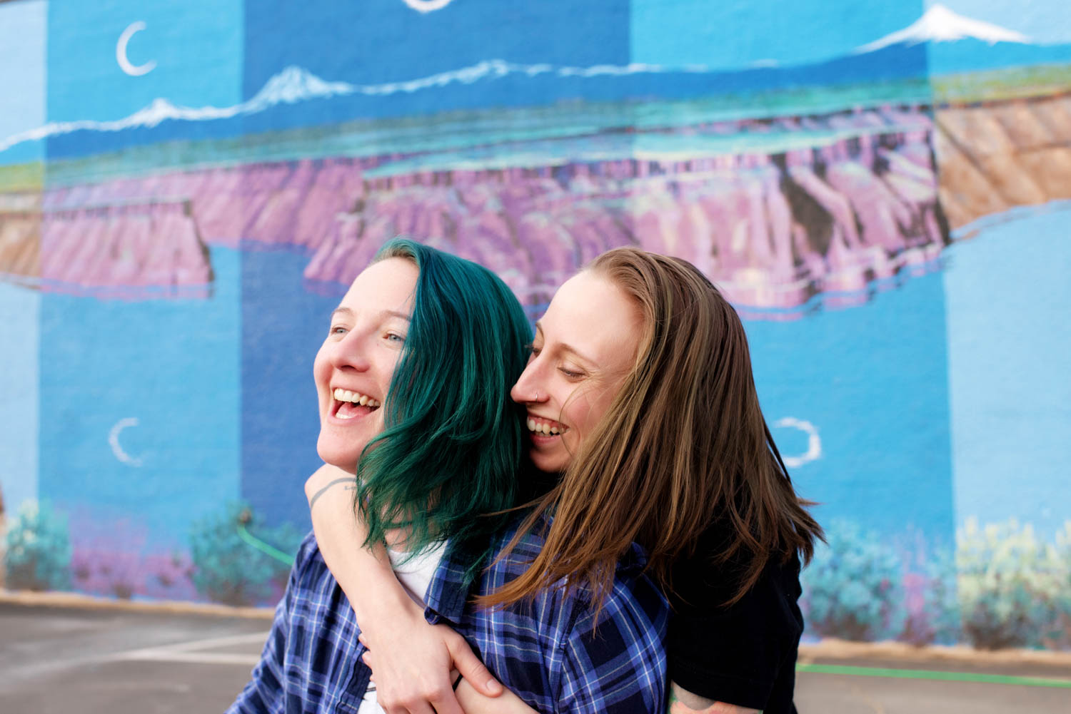 same sex couple laughing in front of a colorful mural during their engagement session